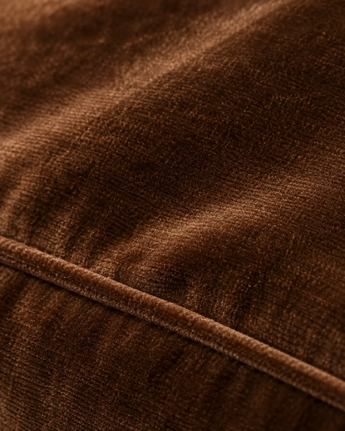 Close detail of the accent chair's tobacco velvet pile and piped seam