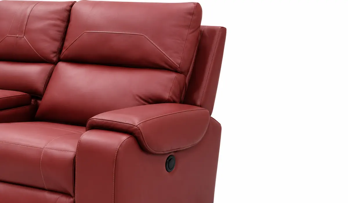 Close detail of the red leather recliner's padded arm, contrast stitch line and the round recline control set into the side panel