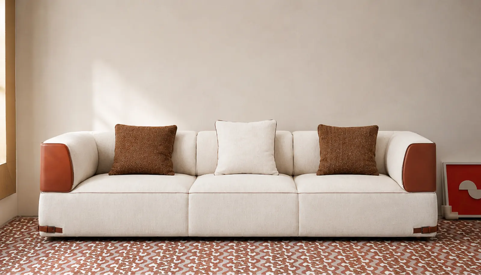 A low three-seat sofa in oatmeal linen with tan leather arm caps and buckle straps, in a warm daylit room over a patterned rust rug