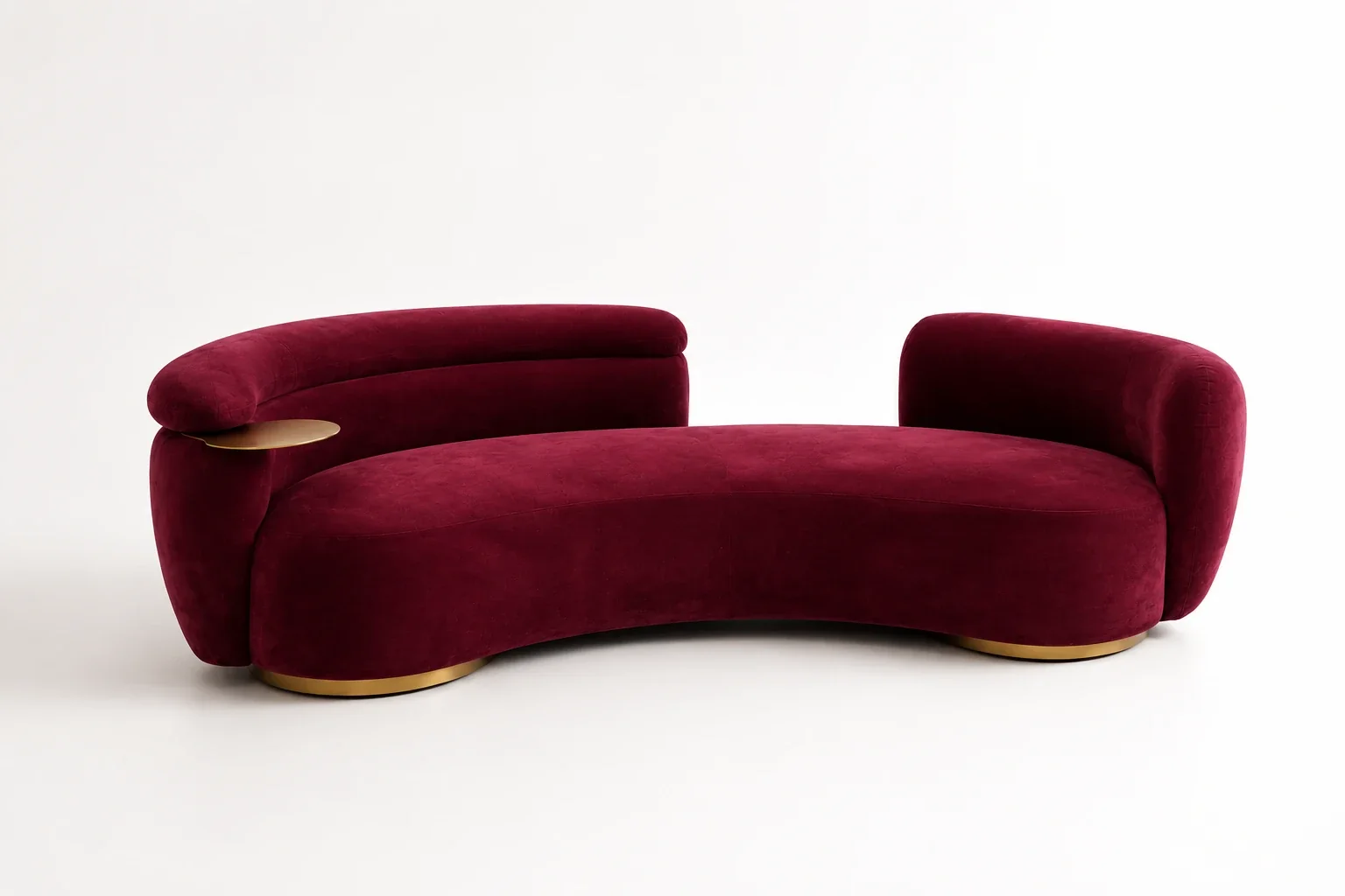 The Curva lounge sofa in burgundy velvet with a brass base and a brass tray at the arm, on a plain studio background
